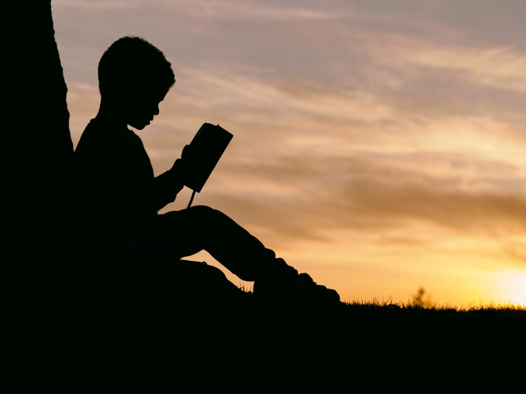 Young boy reading by a tree